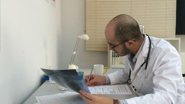 젊은 남자 의사 엑스레이 이미지를 검사 하 고 양식을 작성 집중 — 비디오