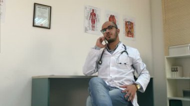 Cep telefonu üzerinde konuşurken ve bakarak genç erkek doktor