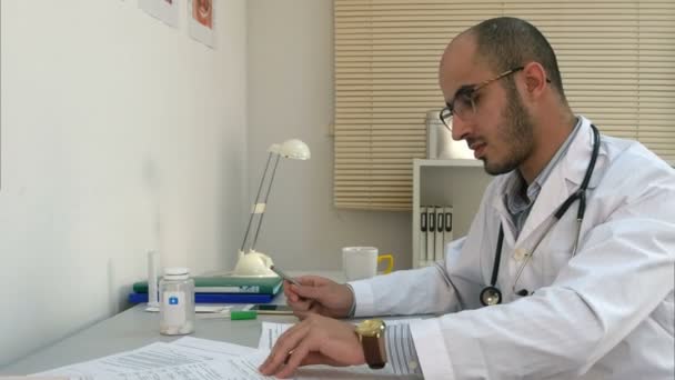 Médico ocupado trabalhando com papéis e conversando por telefone em seu escritório — Vídeo de Stock