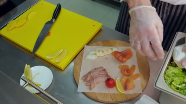 Кухарі руками в рукавичках кладуть салат на дерев'яну тарілку з різним м'ясом — стокове відео