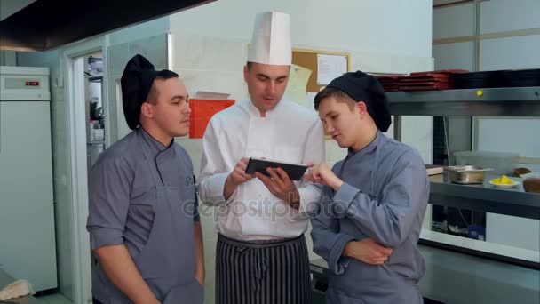 Концентрированный шеф-повар показывает своим ученикам что-то на цифровом планшете — стоковое видео