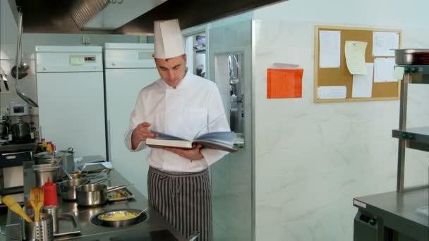 Головний шеф-кухар шукає рецепт у кулінарній книзі під час перевірки свого учня — стокове відео