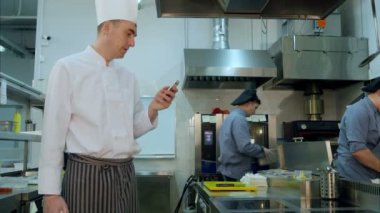 Baş aşçı mutfakta ayakta ve cep telefonunu kullanma