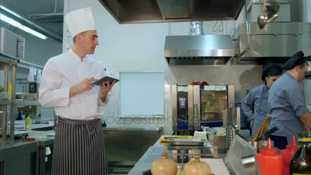 Chef usando tablet digital e assistindo seus trainees cozinhar — Vídeo de Stock