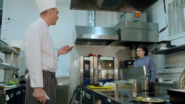 Chef cuisinier lisant les commandes en ligne de son téléphone et donnant des tâches aux cuisiniers — Video