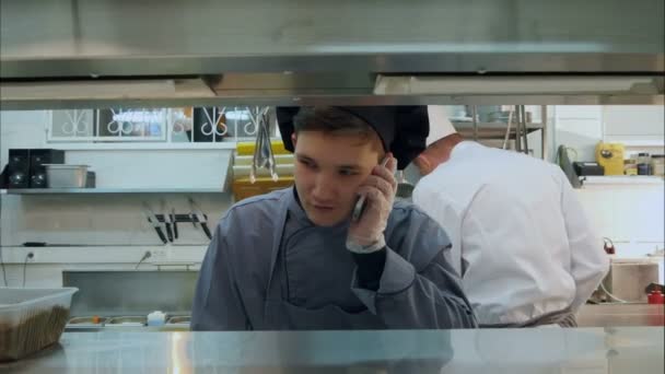 Siswa magang memasak muda berbicara di telepon di dapur profesional — Stok Video
