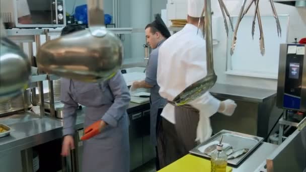 Chef-kok opruimen van de werkplek terwijl zijn stagiairs bezig met hun keuken taken — Stockvideo