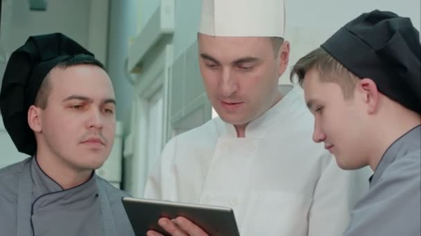 Young cook trainees having discussion with chef holding tablet — Stock Video