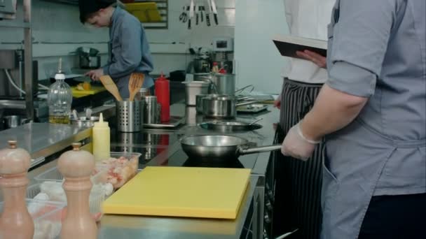 Kepala koki dengan buku resep menonton proses memasak di dapur profesional — Stok Video