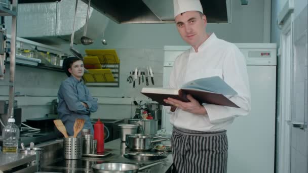 Hombre chef sosteniendo libro de recetas mientras cocinero aprendiz asintiendo con la cabeza aprobadamente — Vídeos de Stock