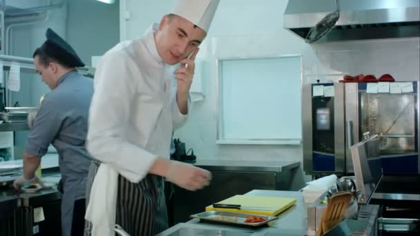 Chef mluvil po telefonu a hodil přísady na pánev v kuchyni restaurace — Stock video