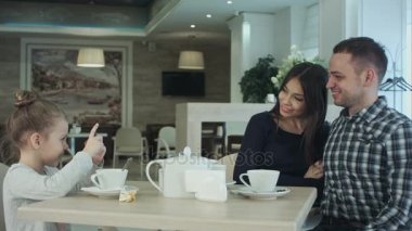 Mutlu anne, baba ve küçük kız cafede akşam yemeği. Çocuk alarak fotoğraf yanında smartphone kameraya poz veliler ise.
