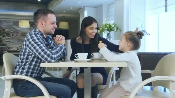 Happy young parents chatting witn daughter during their family vacation in cafe drinking tea. — Stock Video
