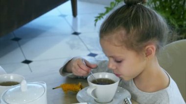 Küçük sarışın kız ailesi tablet ile meşgulken kaşık gelen çay içme.