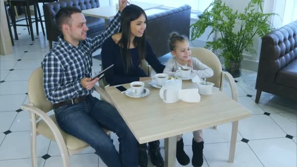 Amistosa familia sentada en la cafetería, sonriendo, posando y simiendo . — Vídeo de stock