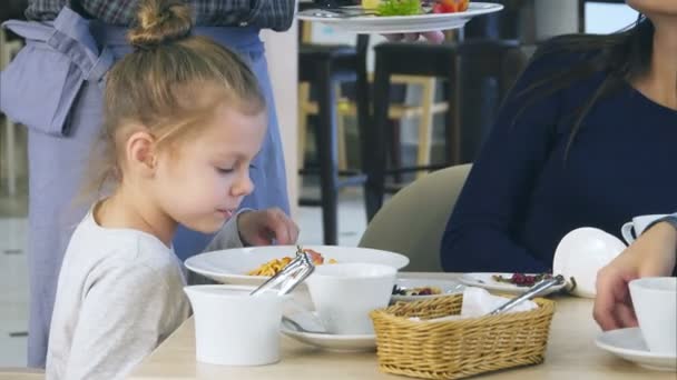 Süßes kleines Mädchen gießt Käse in ihre Spaghetti im italienischen Restaurant, während ihre jungen Eltern ihre Gemüsesalate schon gegessen haben. — Stockvideo