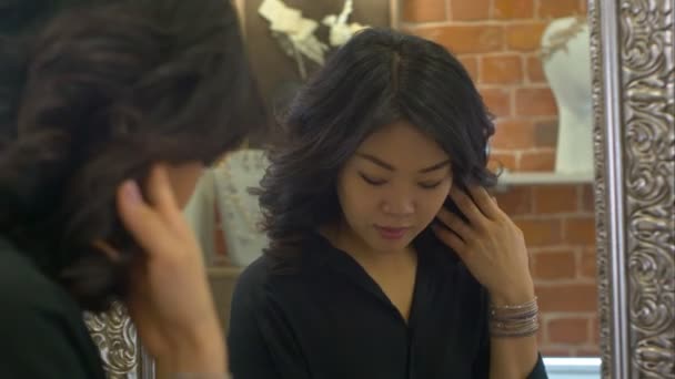 Reflection of an asian woman on a mirror as she tries earrings in a jewellery store — Stock Video