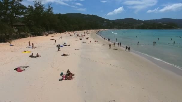 ПХУКЕТ, Таиланд - 20 ЯН 2017: Вид с воздуха на толпу туристов отдыхает на морском пляже возле маленькой деревни в летний солнечный день — стоковое видео