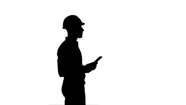 Silhouette Contractor engineer in hardhat inspecting construction site holding digital tablet — Stock Video