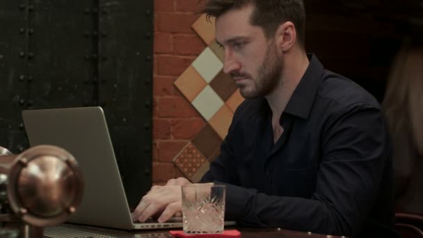 Knappe zakenman werking voort zijn laptop terwijl het hebben van een drankje in een stijlvolle bar — Stockvideo
