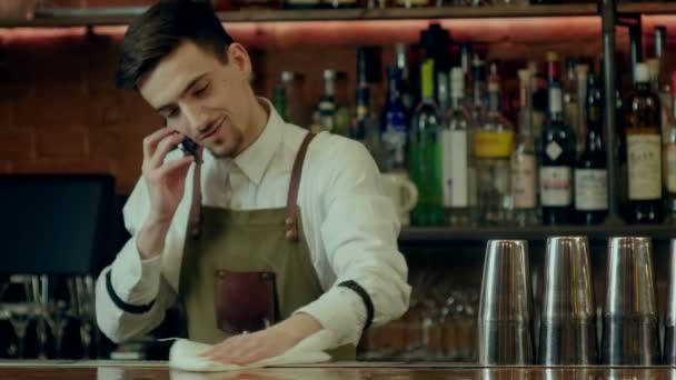 Bartender limpando bar contador e falando via telefone celular — Vídeo de Stock