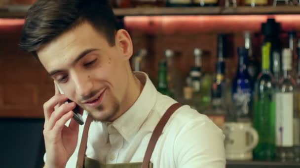 Glad bartendern i förkläde uppmanar smartphone på bar — Stockvideo