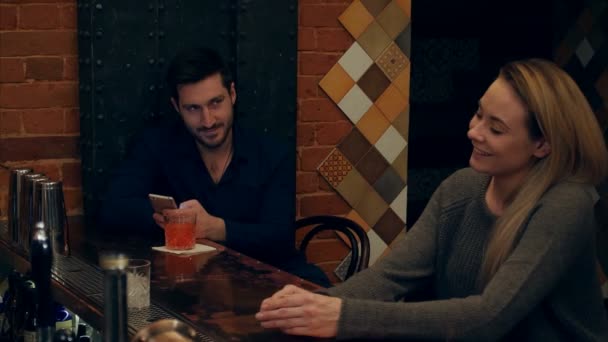 Man använder en smartphone och stirrar på unga vackra kvinnan bakom honom, medan bartender förbereder en cocktail i en bar — Stockvideo