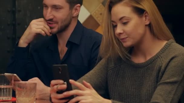 Νεαρό ζευγάρι χρησιμοποιούν κινητά τηλέφωνα και λαμβάνοντας funnie selfie φωτογραφία που κάθεται στο καφενείο — Αρχείο Βίντεο