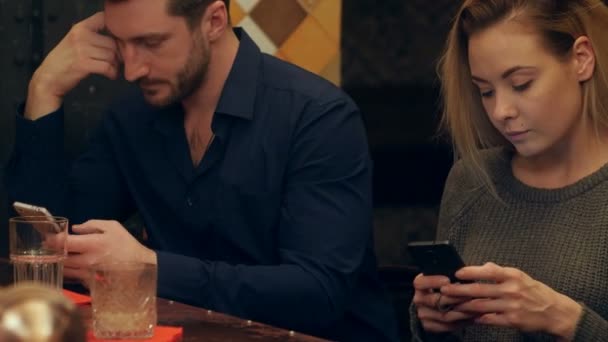 英俊的男人和有魅力的女人使用 smartphohes，坐在一间酒吧 — 图库视频影像