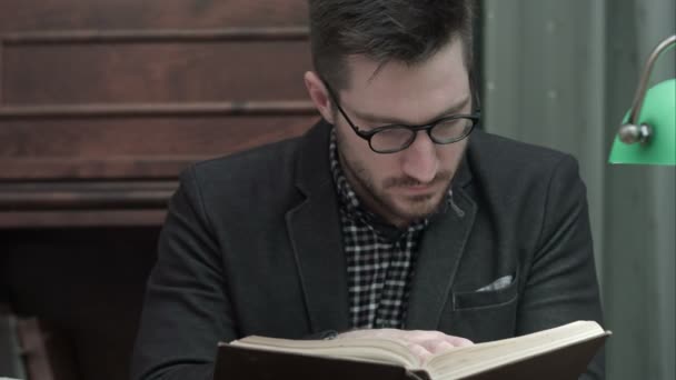 Jovem acadêmico em óculos atentamente lendo um livro — Vídeo de Stock
