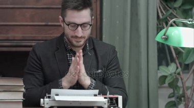 Ellerini ovuşturarak ve kırmızı bir vintage daktiloda yazmaya başlayan gözlüklü genç yazar