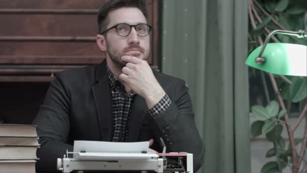 Pensive writer sitting in front of typewriter thinking of new ideas for his book — Stock Video