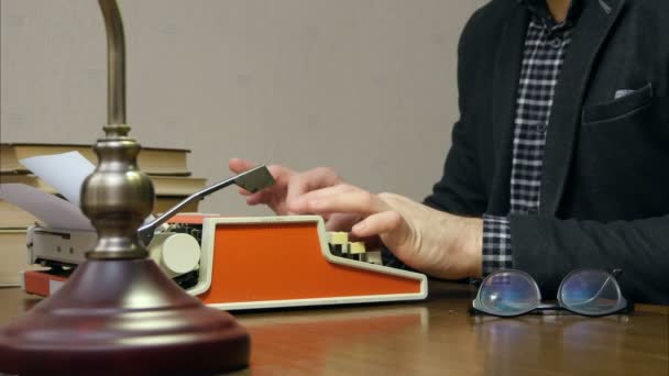 Escritor trabajando en la máquina de escribir en el escritorio con libros y gafas — Vídeos de Stock