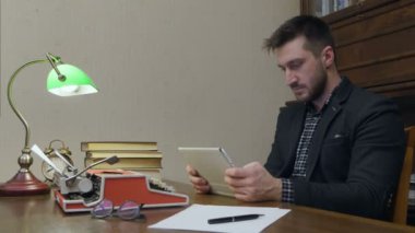 Erkek araştırmacı dijital tablet kitaplar ve daktilo ile çalışma masasında oturan kullanma