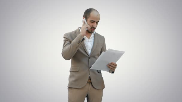 Mladý muž v obleku mluvil po telefonu a držení papíry na bílém pozadí. — Stock video