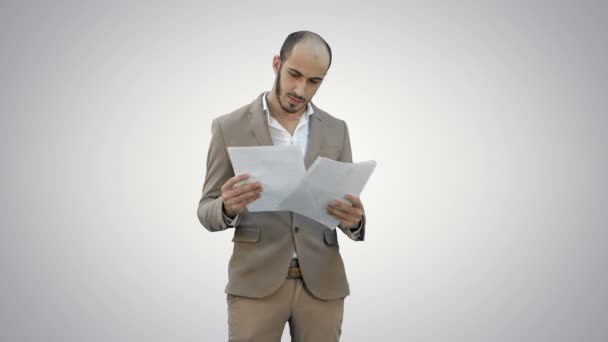 Grave giovane uomo d'affari in piedi e la lettura di alcuni documenti su sfondo bianco . — Video Stock