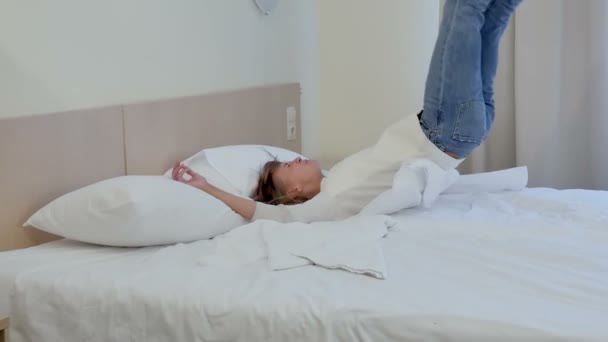 Смеющаяся женщина падает в постель и играет с подушками — стоковое видео
