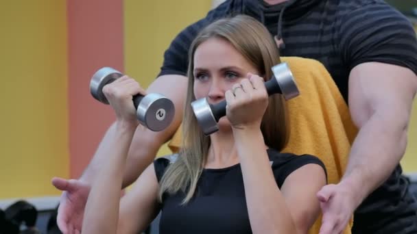 Mujer con su entrenador personal en el gimnasio haciendo ejercicio con pesas — Vídeo de stock