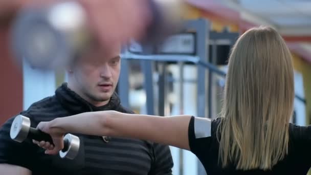 Персональный тренер наблюдает за молодой женщиной с помощью штанги в спортзале — стоковое видео