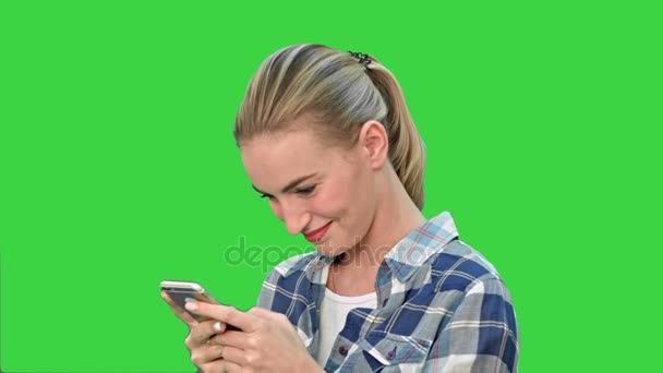 Ung kvinna ler medan textilen ett meddelande via mobilen på en grön skärm, Chroma Key. — Stockvideo