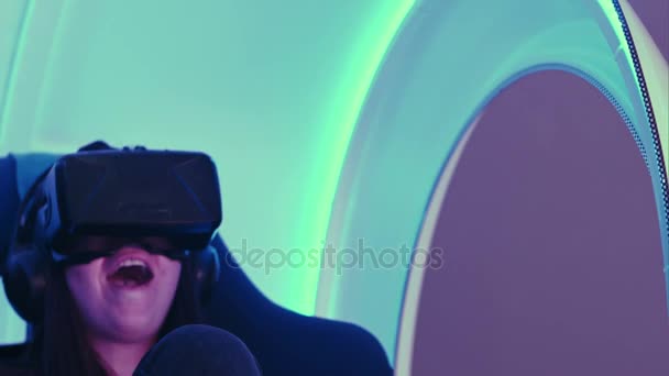 Chica sorprendida experimentando la realidad virtual en una silla interactiva en movimiento — Vídeos de Stock