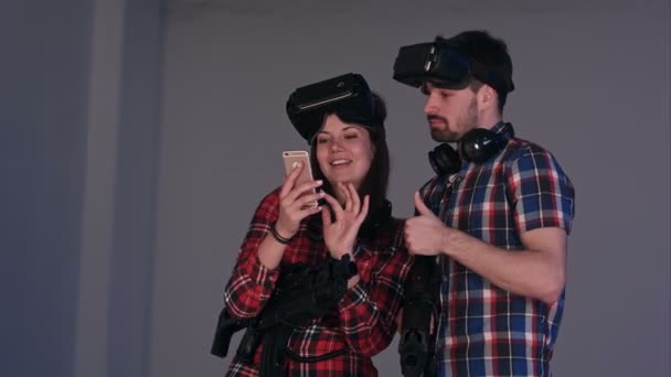 Laughing couple in virtual reality headsets looking at their funny photos on the phone — Stock Video