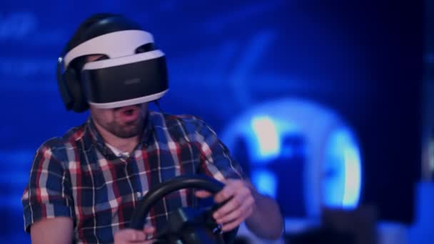 Felice giovane uomo in cuffia realtà virtuale giocare videogame con ruota da corsa — Video Stock