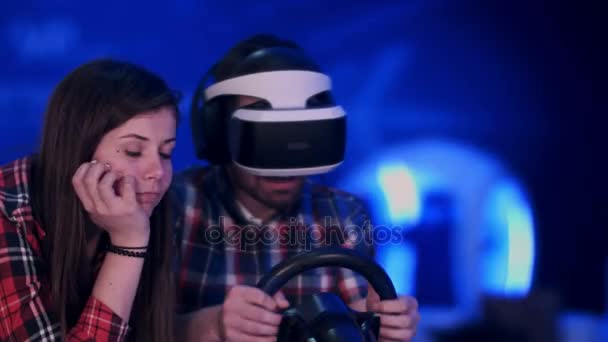 Menina levemente entediada assistindo seu namorado animado jogando jogo de corrida no fone de ouvido vr — Vídeo de Stock