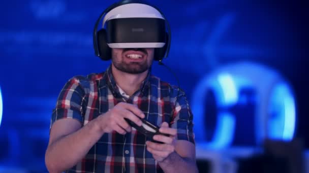 Χαρούμενος νεαρός άνδρας με το σετ κεφαλής εικονικής πραγματικότητας με το gamepad ελεγκτή παίζει βιντεοπαιχνίδι αγώνων — Αρχείο Βίντεο