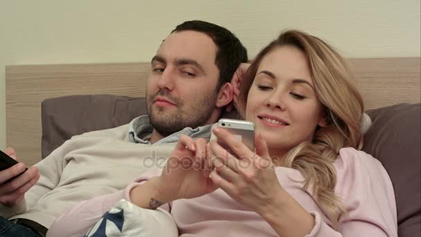 Belle femme couchée au lit textant au téléphone portable souriant, tandis que son partenaire s'incruste à l'écran — Video