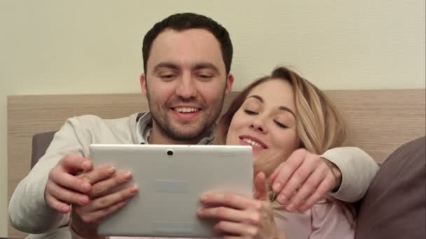 Genç çift yatakta dijital tablet, gülümseyen ve gülerek kullanın — Stok video