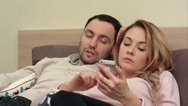 戦うため夜ベッドでと主張し、若いカップル女性テキスト メッセージのスマート フォンを使用している人 — ストック動画