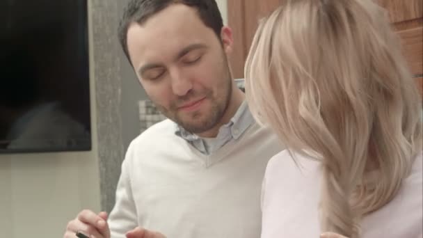 Молодая пара слушает музыку через смартфон, разговаривает на кухне — стоковое видео