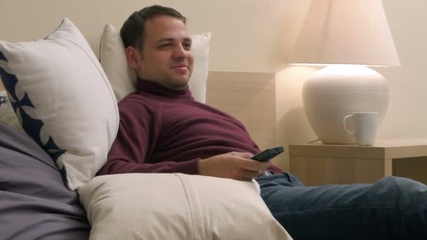 Зрілий красивий чоловік розслабляється у своїй кімнаті готелю шукає щось дивитися по телевізору — стокове відео